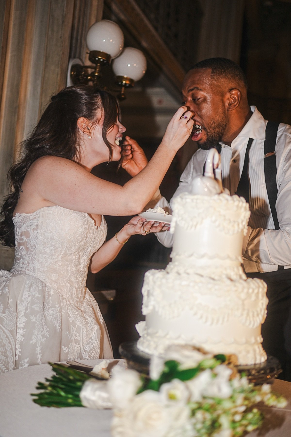 Bride feeding the groom a bite of wedding cake, both laughing