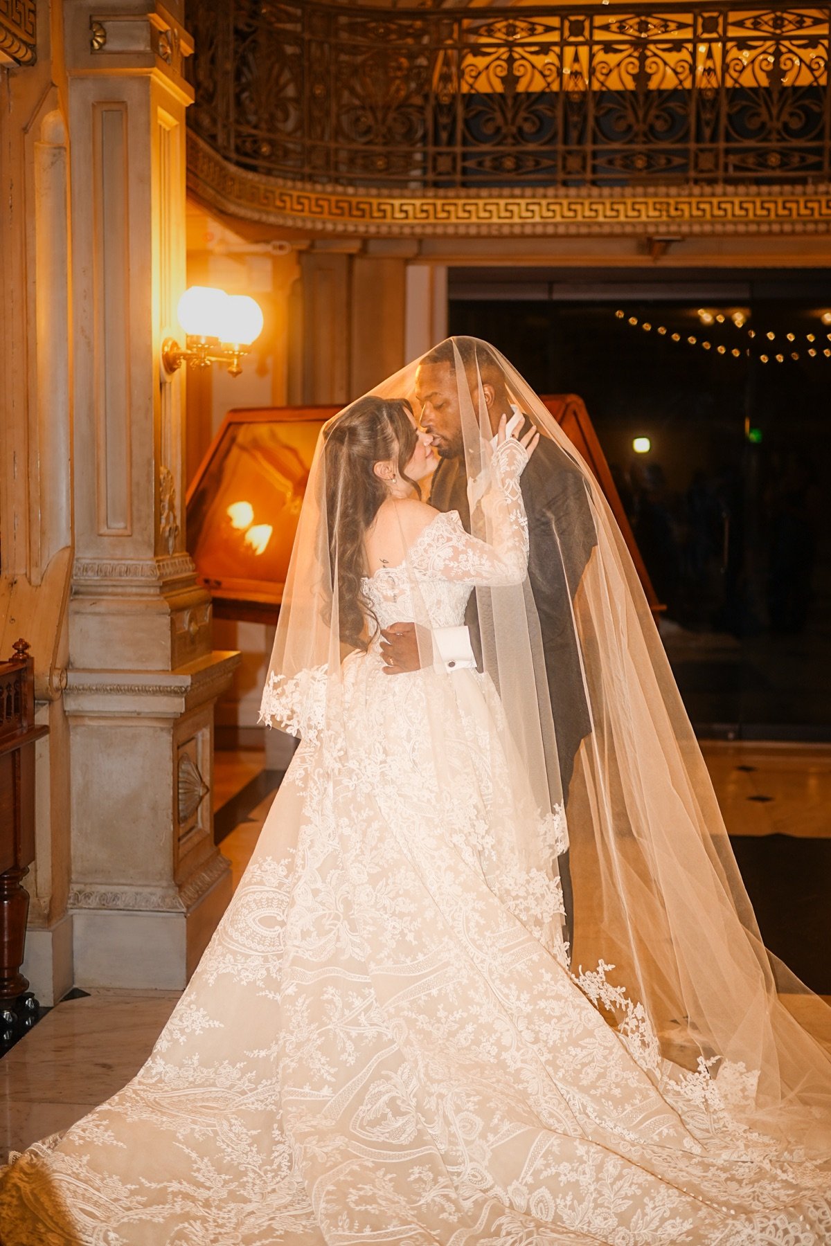 Bride and groom kissing under her veil in warm lamplight